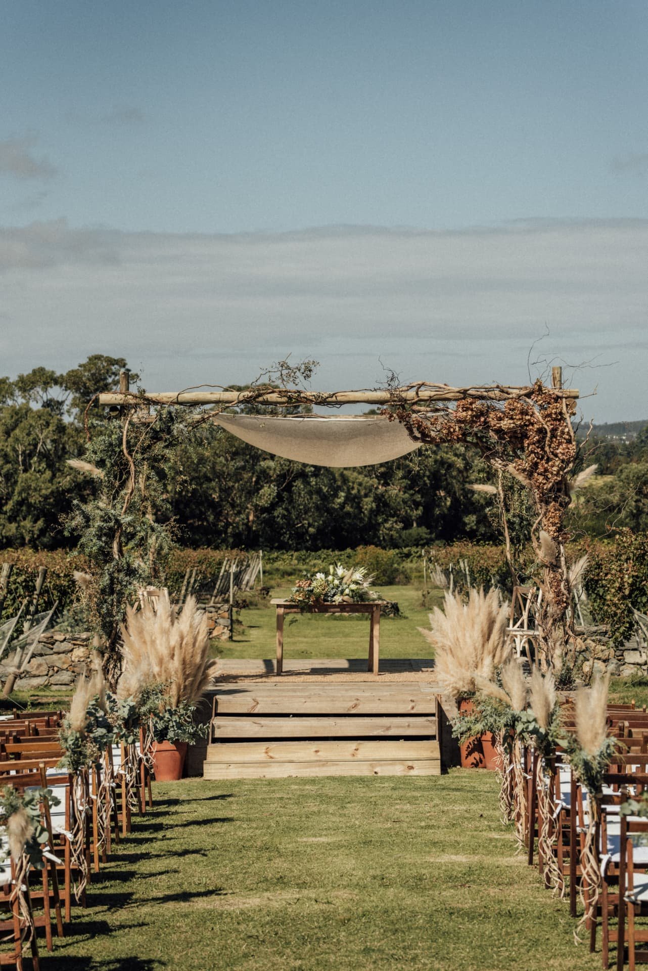 Cerimônia ao ar livre decorada com capim-dos-pampas entre vinhedos